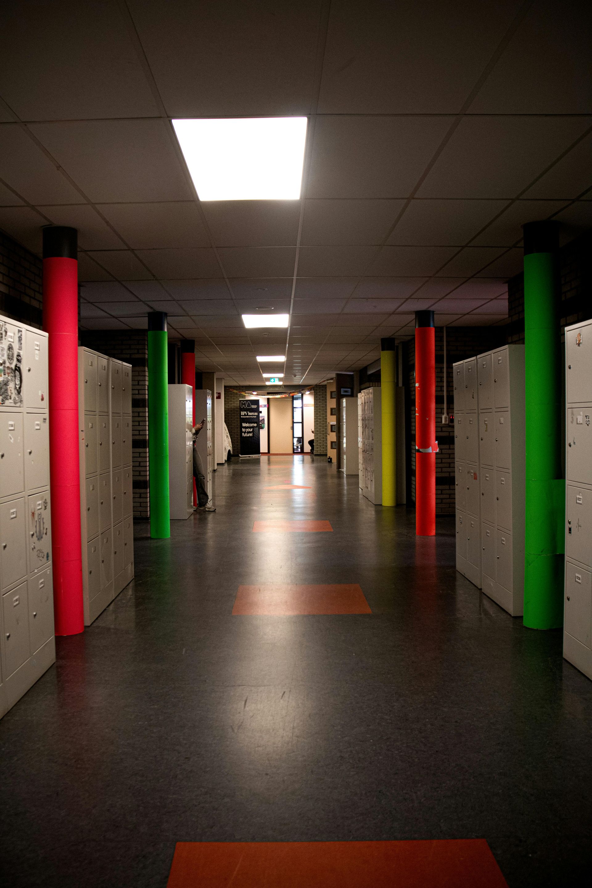 Lege gang met rode en groene pilaren, tl-plafondverlichting en een reflecterende vloer.