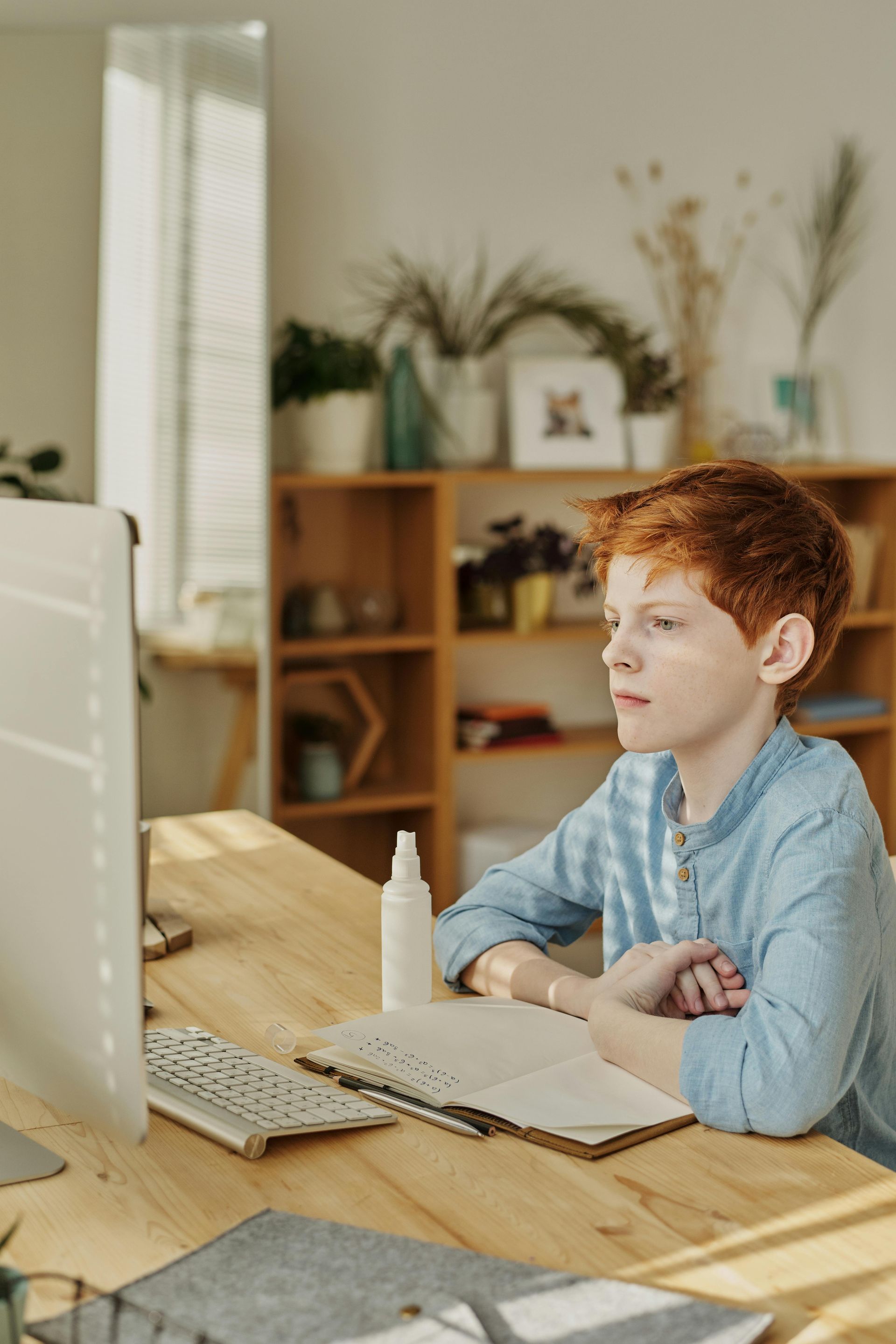 Een persoon werkt aan een bureau met een laptop en notitieboek in een lichte thuiswerkplek.