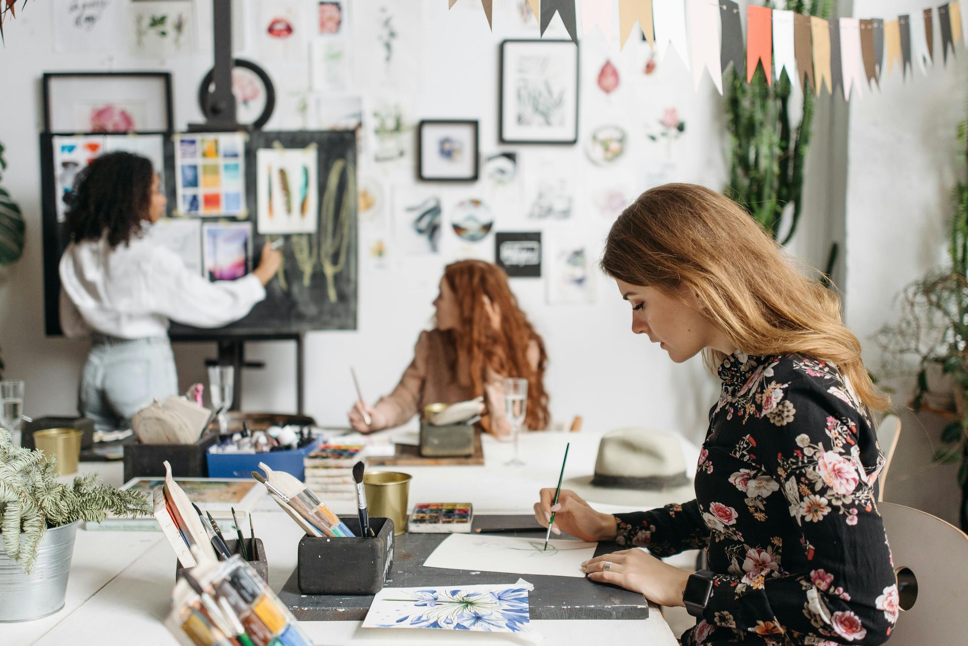 Mensen knutselen aan een felverlichte kunststudiotafel, omringd door verf, papier en muurdecoratie.