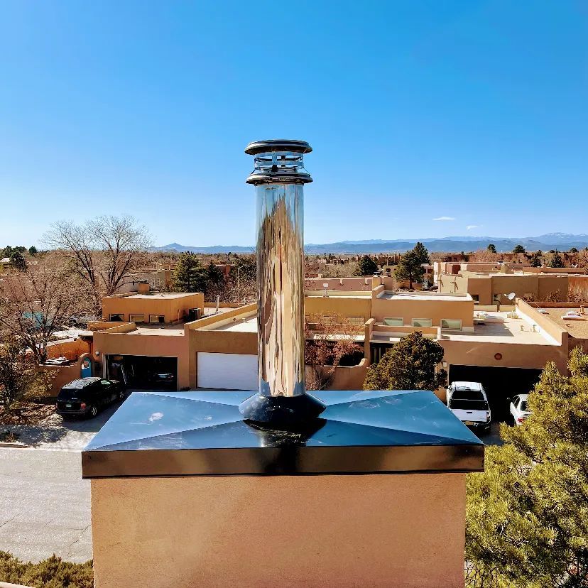 Chrome vent pipe on a rooftop with desert buildings and mountains under a blue sky