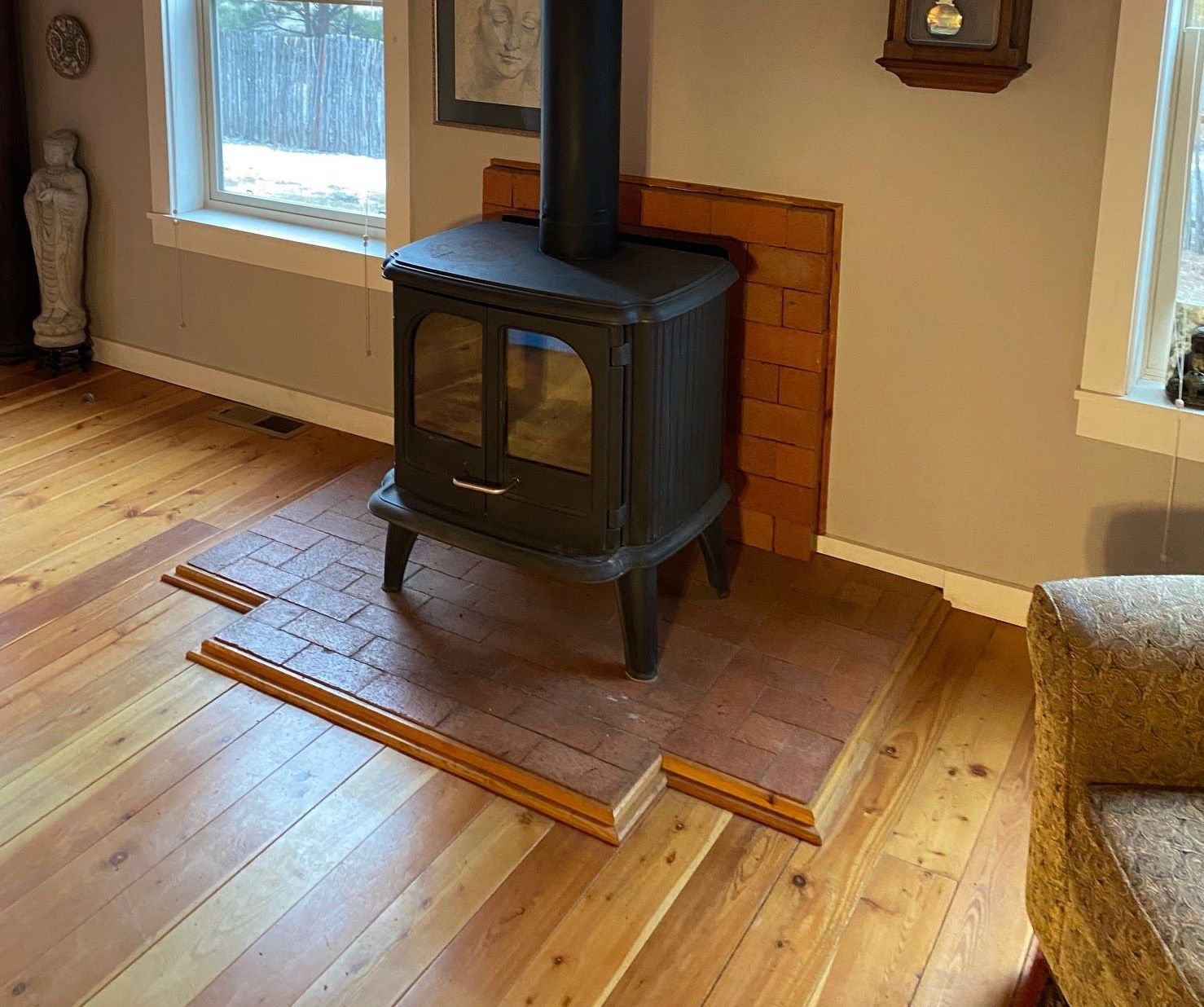 A black wood-burning stove sits on a brick hearth in a room with hardwood floors and windows.
