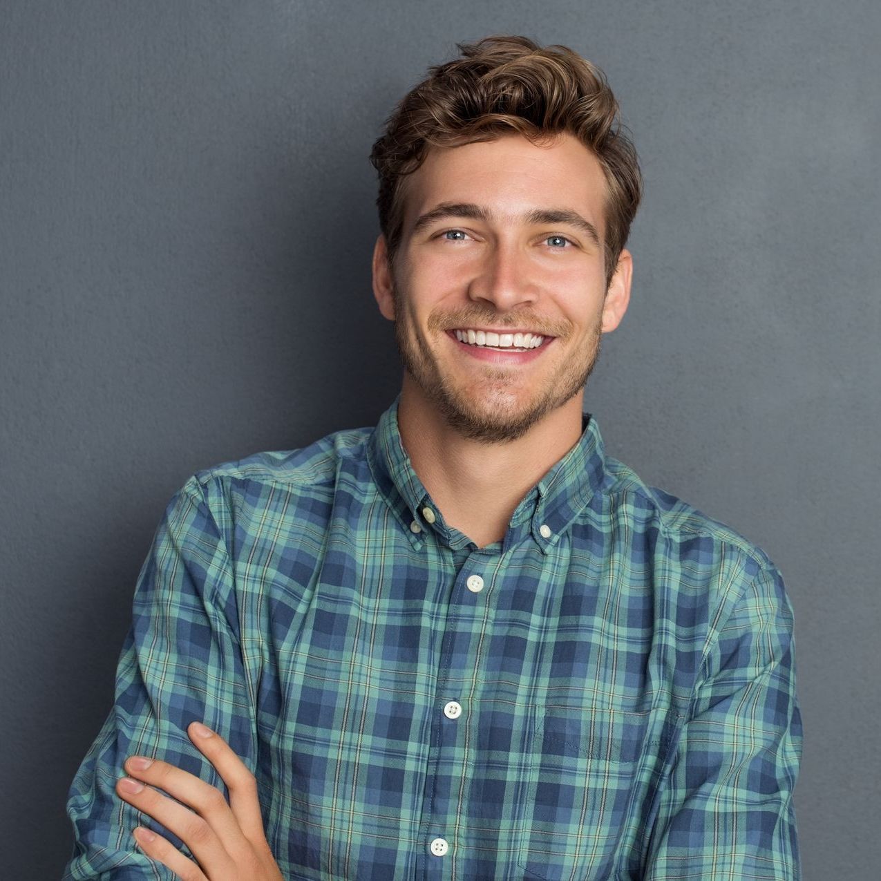 A man in a plaid shirt is smiling with his arms crossed.