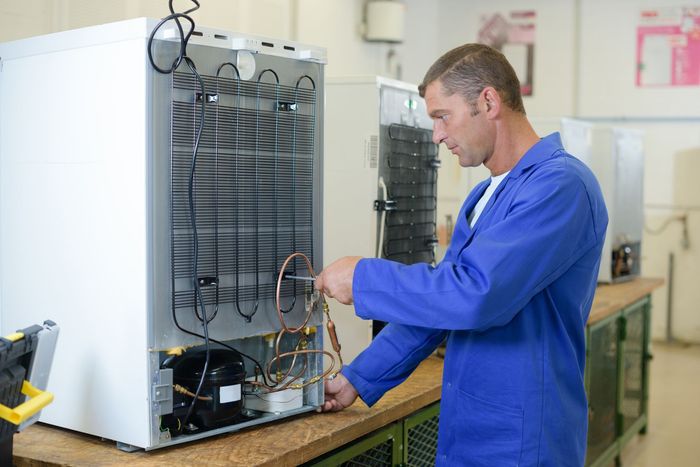 A man is working on a refrigerator in a workshop.