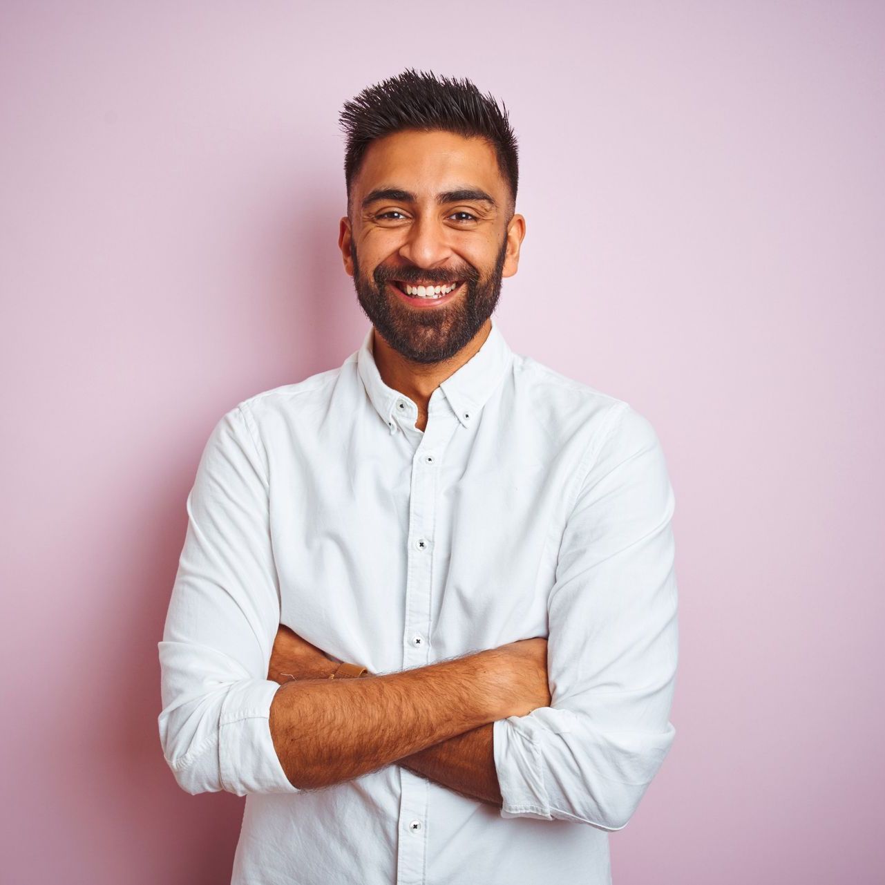 A man with a beard is standing with his arms crossed and smiling.