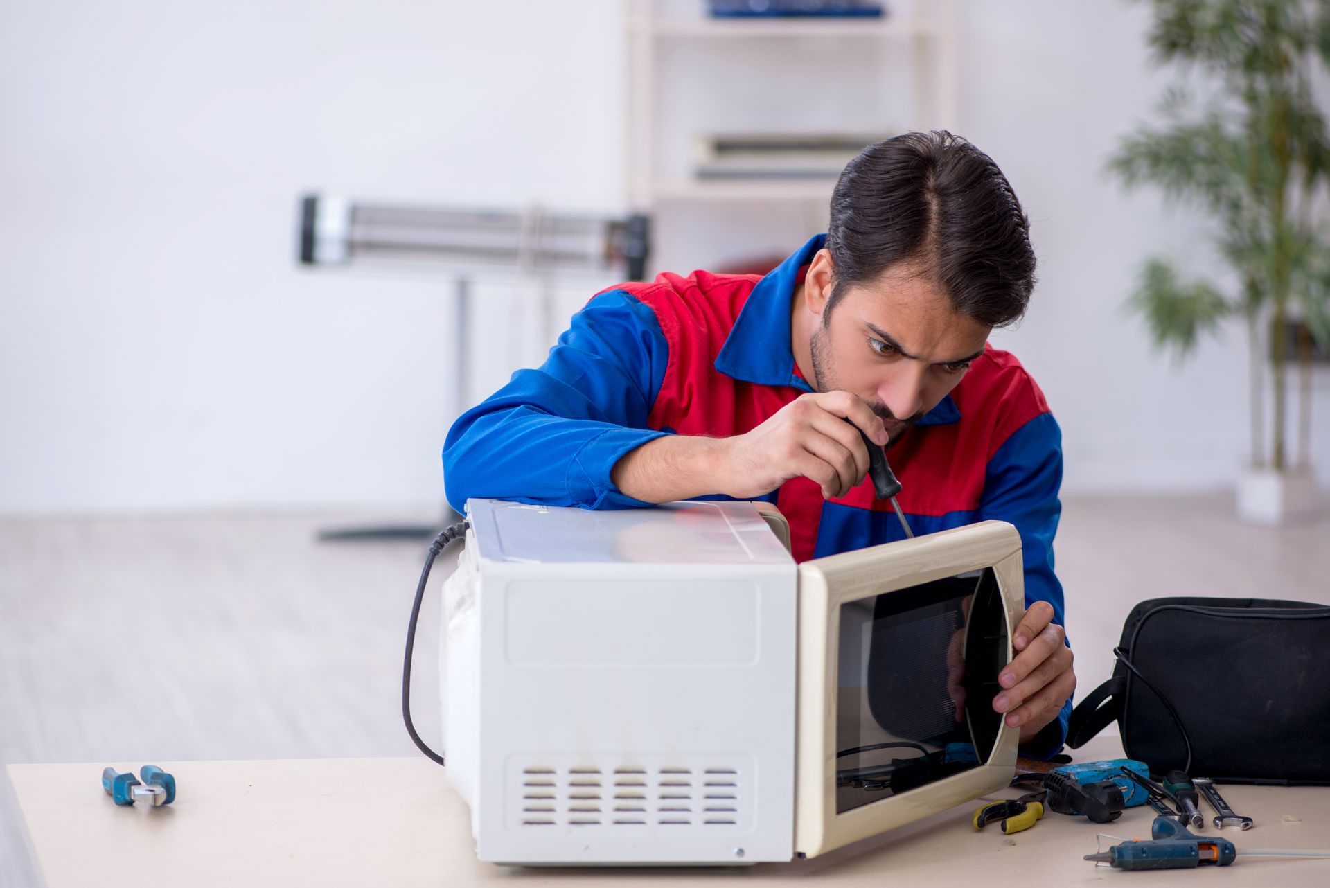 A man is fixing a microwave oven with a screwdriver.