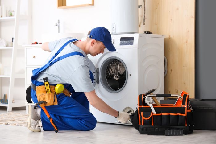 A man is kneeling on the floor fixing a washing machine.