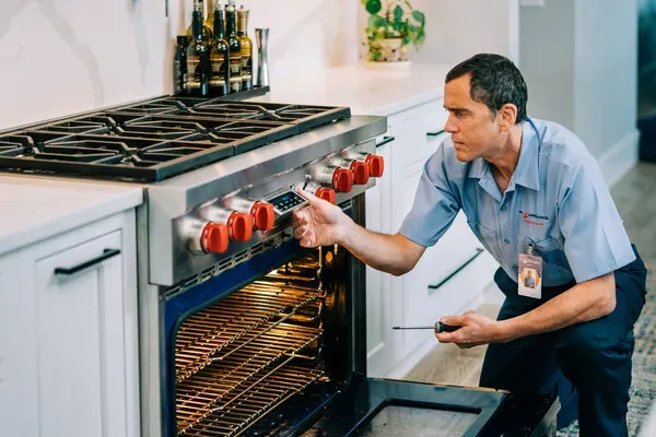 A man is working on a stove in a kitchen.
