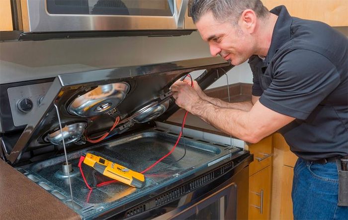 A man is fixing a stove in a kitchen.