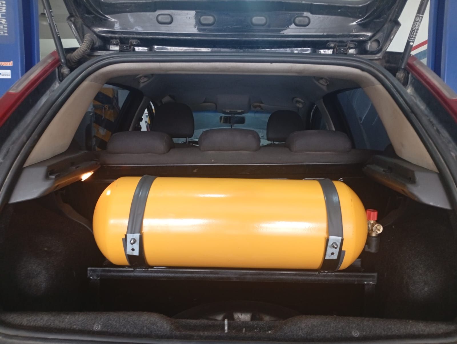 Cilindro de gas naranja asegurado en el área de carga de un SUV con el portón trasero abierto.