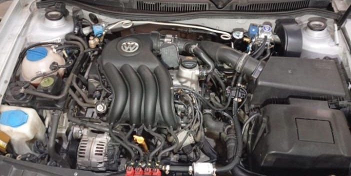 Compartimento del motor del coche con emblema de Toyota, colector de admisión negro, batería y depósitos de refrigerante.