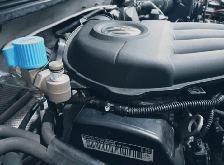 Compartimento del motor del coche con tapón azul del líquido limpiaparabrisas y cubierta del motor negra.