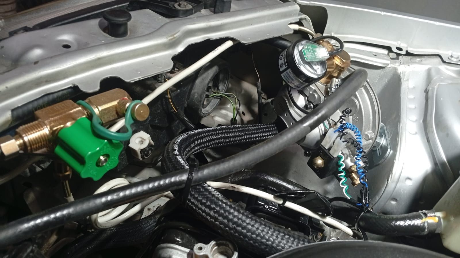 Compartimento del motor del coche con mangueras, cableado y componentes metálicos expuestos.