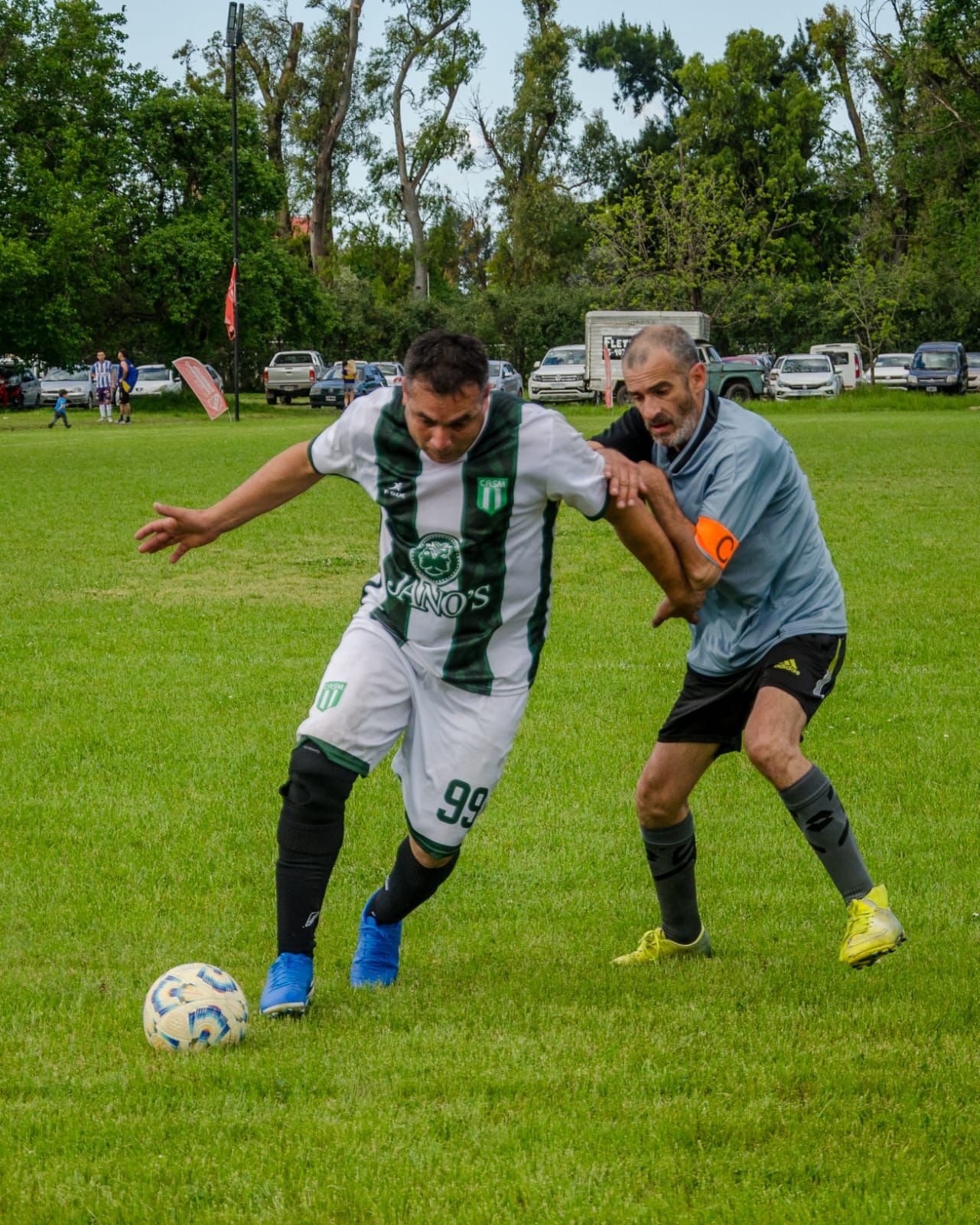 Dos jugadores de fútbol compiten por el balón en un campo de césped, y uno de ellos, dribla hacia adelante.
