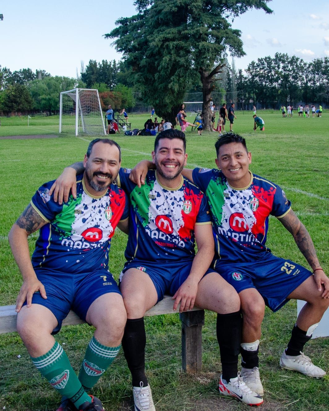 Tres compañeros de equipo con uniformes de fútbol iguales se sientan en un banco en un campo