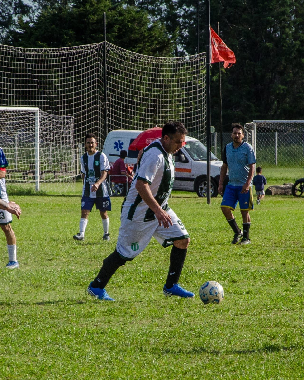 Un jugador de fútbol con una camiseta blanca y negra dribla un balón en un campo de césped durante un partido