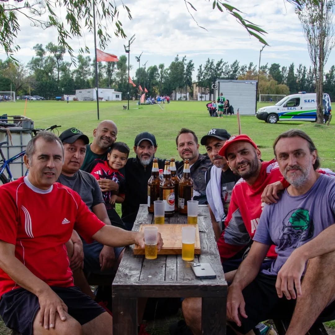 Un grupo de personas sentadas en una mesa de madera al aire libre en un campo de hierba, bebiendo cerveza