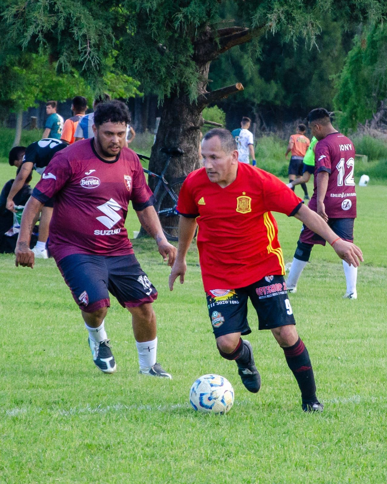 Dos jugadores de fútbol con camisetas rojas compiten por el balón en un campo de césped