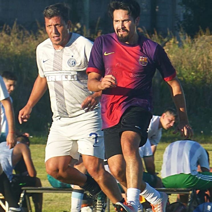 Dos hombres con diferentes camisetas de fútbol corren por un campo de césped durante un partido.