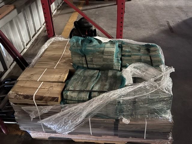 Stacked bundles of strapped cash on a pallet in a warehouse aisle, wrapped in plastic.