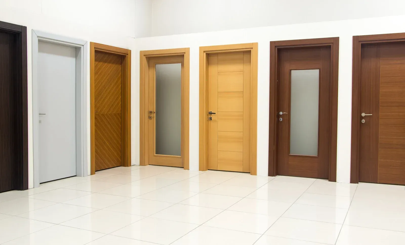 A showroom display of six interior doors in various wood finishes and styles, some with glass panels, on a white floor.