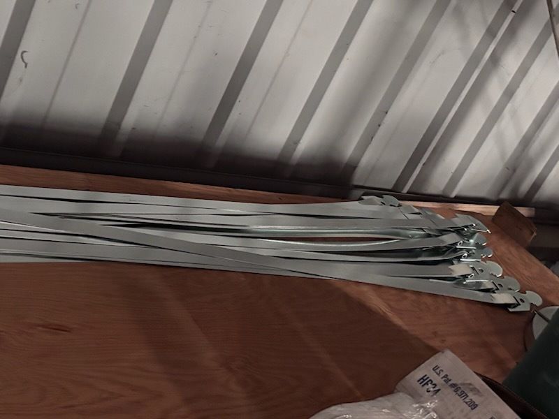Stack of silver metal utensils or tools on a wooden surface under a corrugated roof