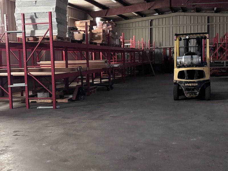 Warehouse interior with red metal shelving and a yellow forklift on a concrete floor
