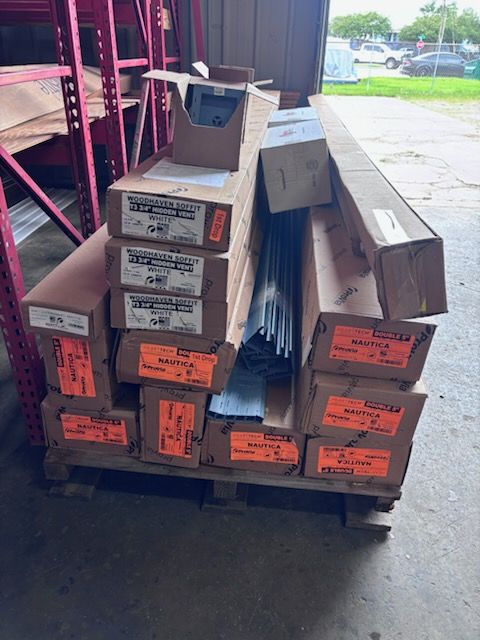Stacked boxed flooring materials on a pallet in a warehouse doorway, with gray carpet strips visible.