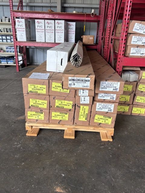 Pallet of boxed PVC pipe fittings in a warehouse aisle, with red metal shelving in the background