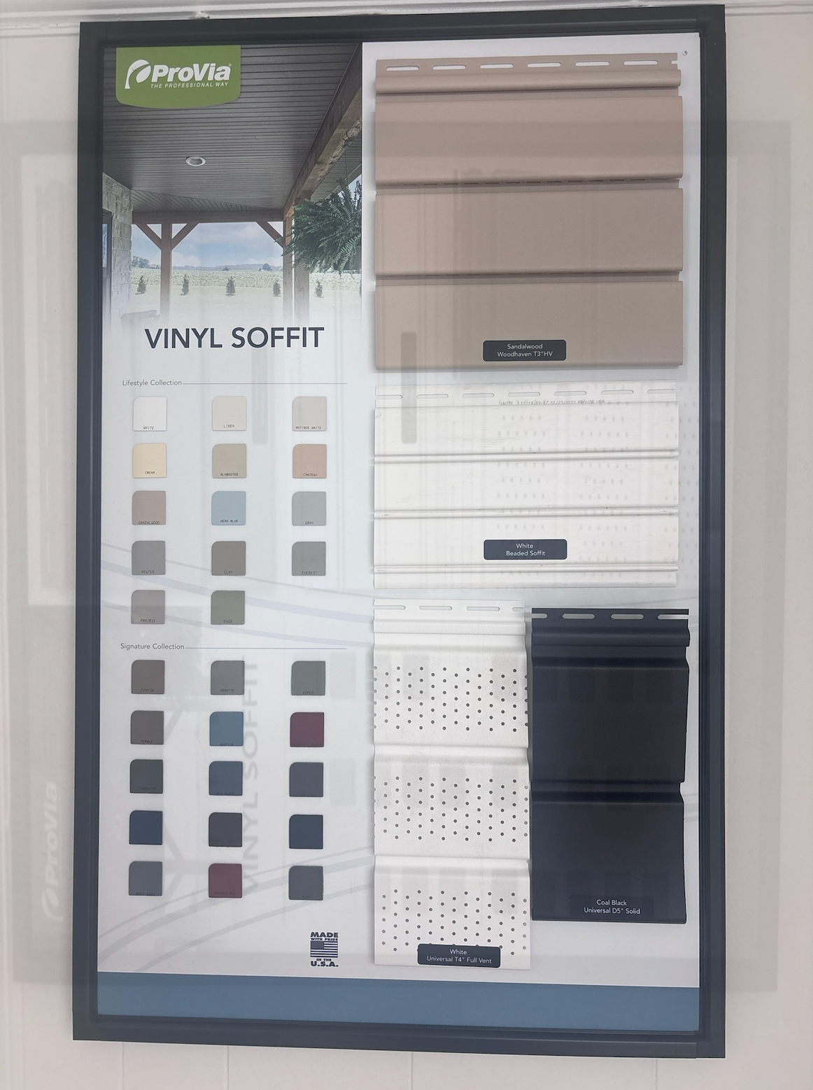 Vinyl soffit display board with sample panels in beige, white, and black on a wall-mounted poster.
