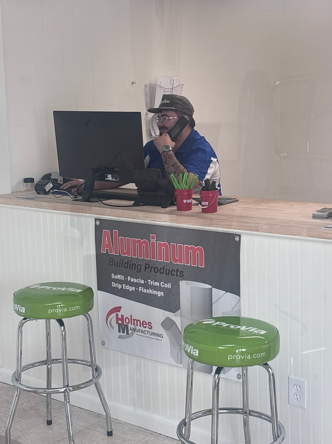 Person seated behind a counter in a small office, wearing a mask and talking on a phone.