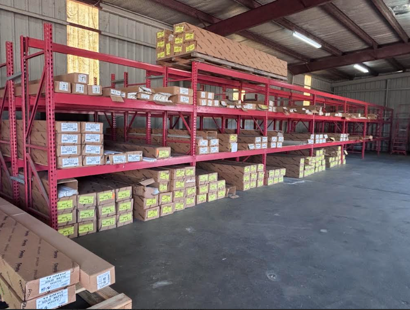 Warehouse with red metal shelving stocked with boxes and cartons under a high ceiling.
