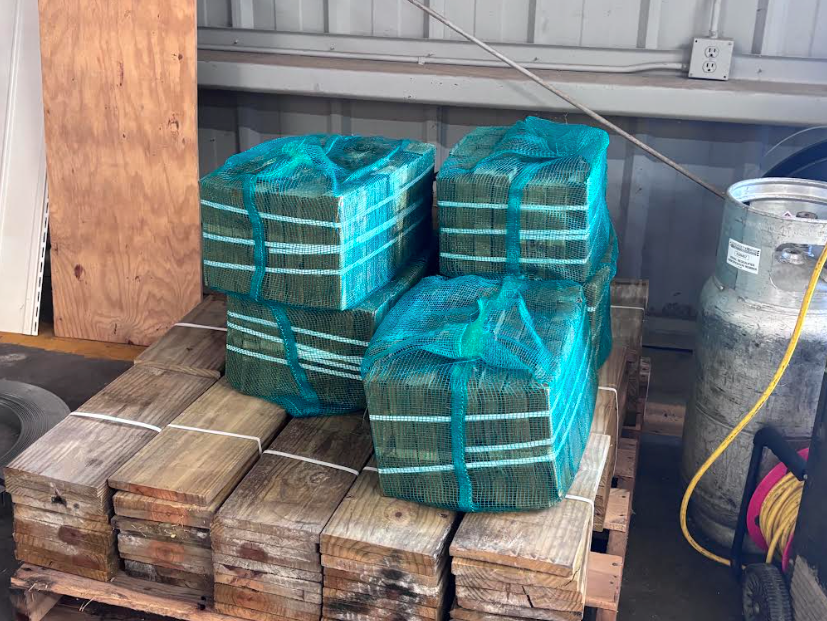 Stacked pallets of green-wrapped bundles and wood blocks inside a warehouse corner.