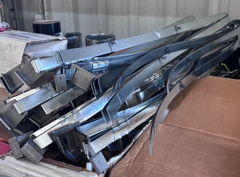 Piled metal beams and ductwork stacked in a room beside a large cardboard box
