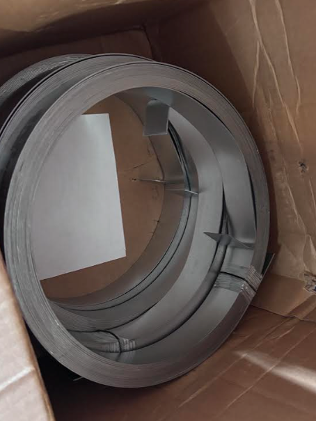 Coiled gray metal duct or vent ring inside a cardboard box, with a white insert panel.