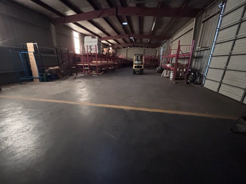 Empty warehouse with concrete floor, metal racks, and a forklift near a large roll-up door