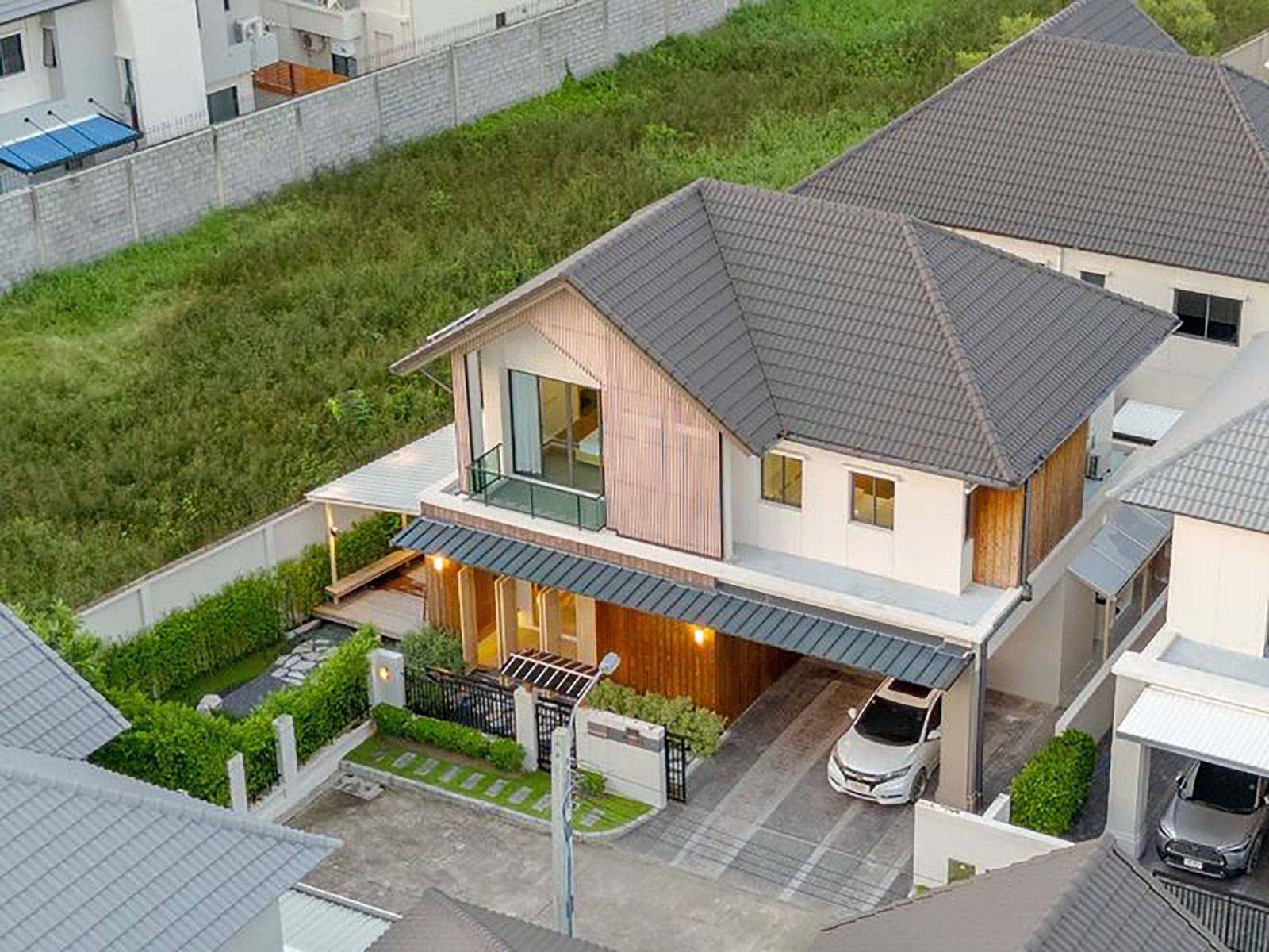 An elevated view of a modern two-story suburban house with a dark tiled roof, wooden siding, and a driveway with a car.