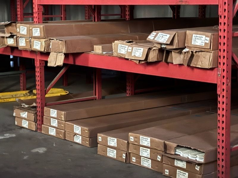 Stacked brown metal beams on red warehouse racks, with labels on the beam ends.