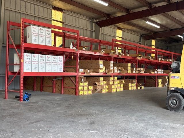 Warehouse with red shelving holding stacked boxes and a yellow forklift on the right