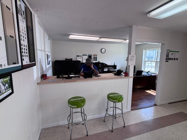 Small office reception area with a person behind the counter and two green stools in front.