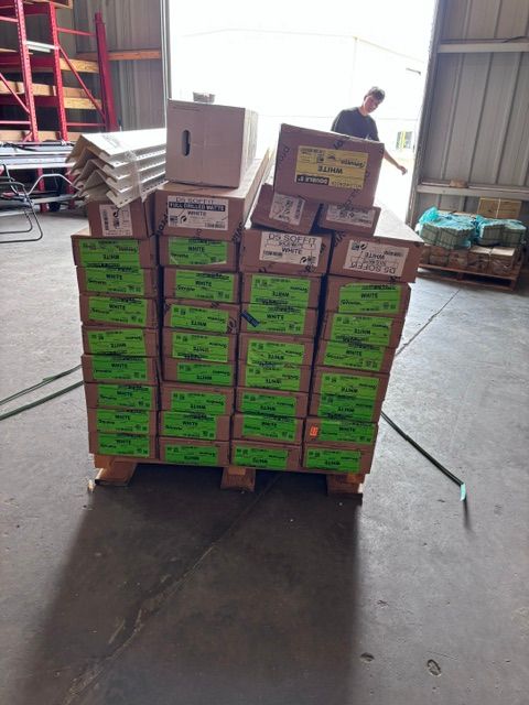 Pallet stacked with green and purple boxed goods in a warehouse, with a worker in the background.