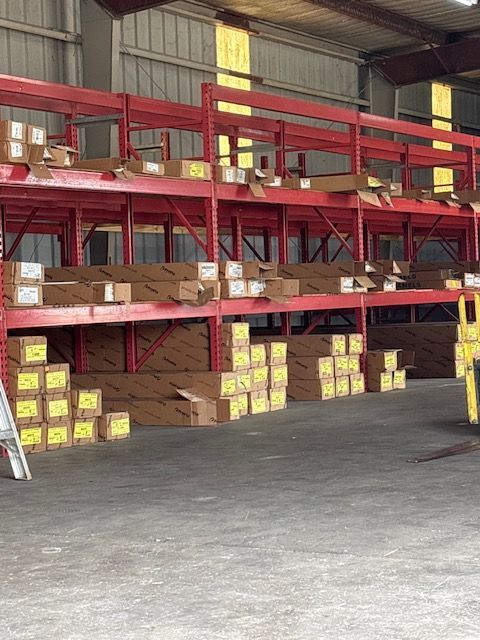 Warehouse shelves with stacked cardboard boxes and yellow-labeled packages under a red metal mezzanine.