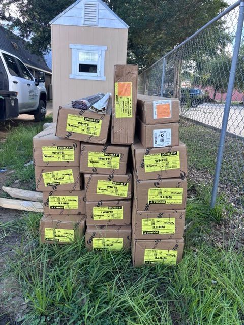 Stack of boxed packages beside a chain-link fence and small shed in a grassy yard.