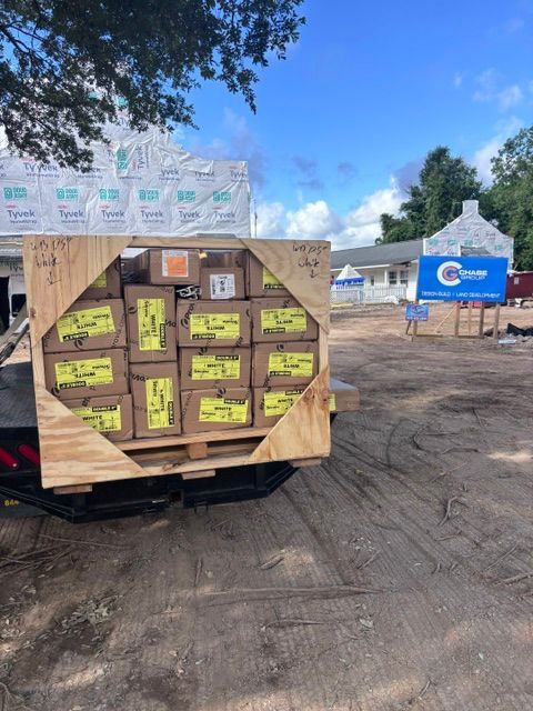 Outdoor pallet of boxed supplies with yellow labels, near a blue sign under a sunny sky