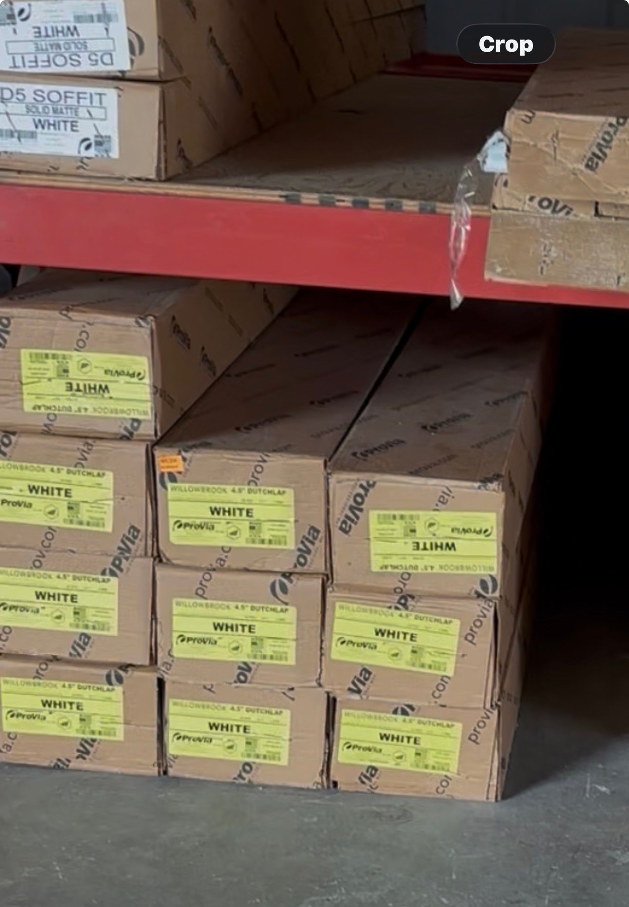 Stacked cardboard boxes on a warehouse shelf, many labeled with yellow tags.