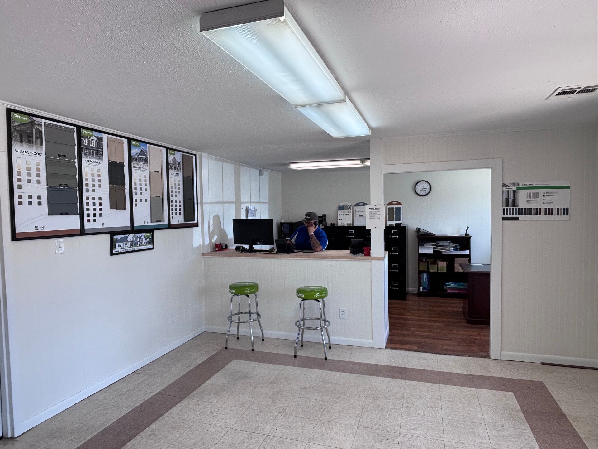 Empty office lobby with reception counter, two stools, wall notices, and an open doorway to a back room