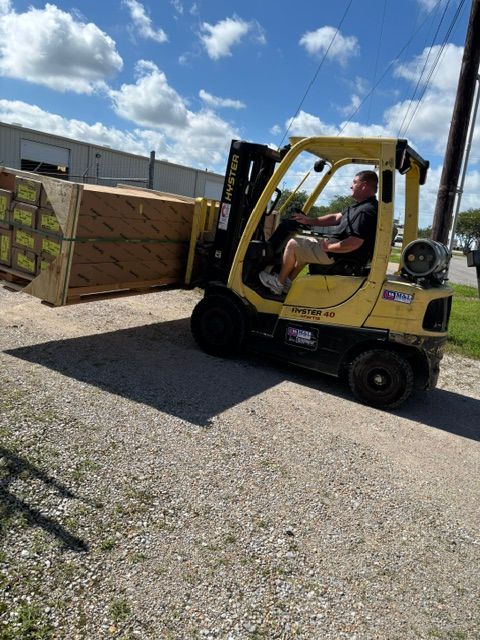 Yellow forklift carrying wooden crates in a gravel yard under a blue sky