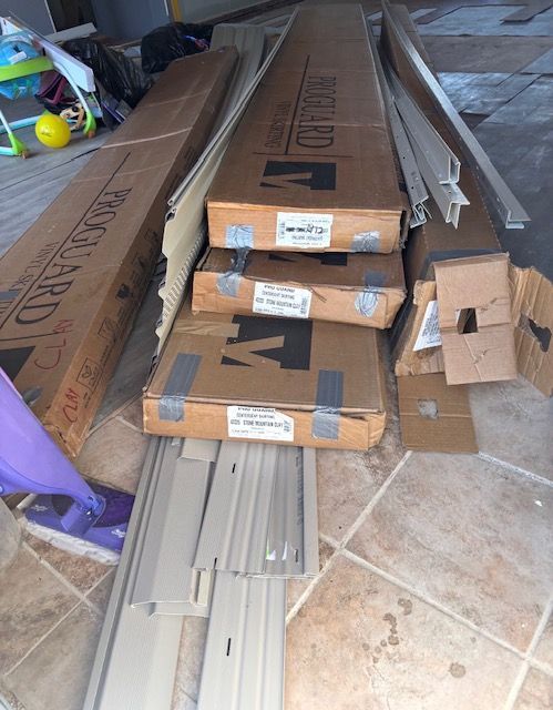 Stacked cardboard boxes and long trim pieces on a tiled floor in a cluttered storage area