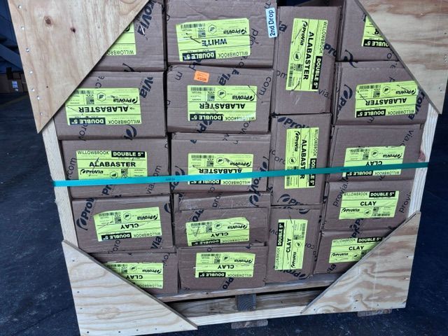 Stacked brown cardboard boxes with green labels strapped inside a wooden crate