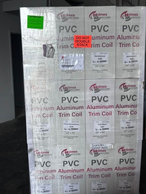 Stacked rolls of silver PVC aluminum trim coil with printed labels and a green sticker
