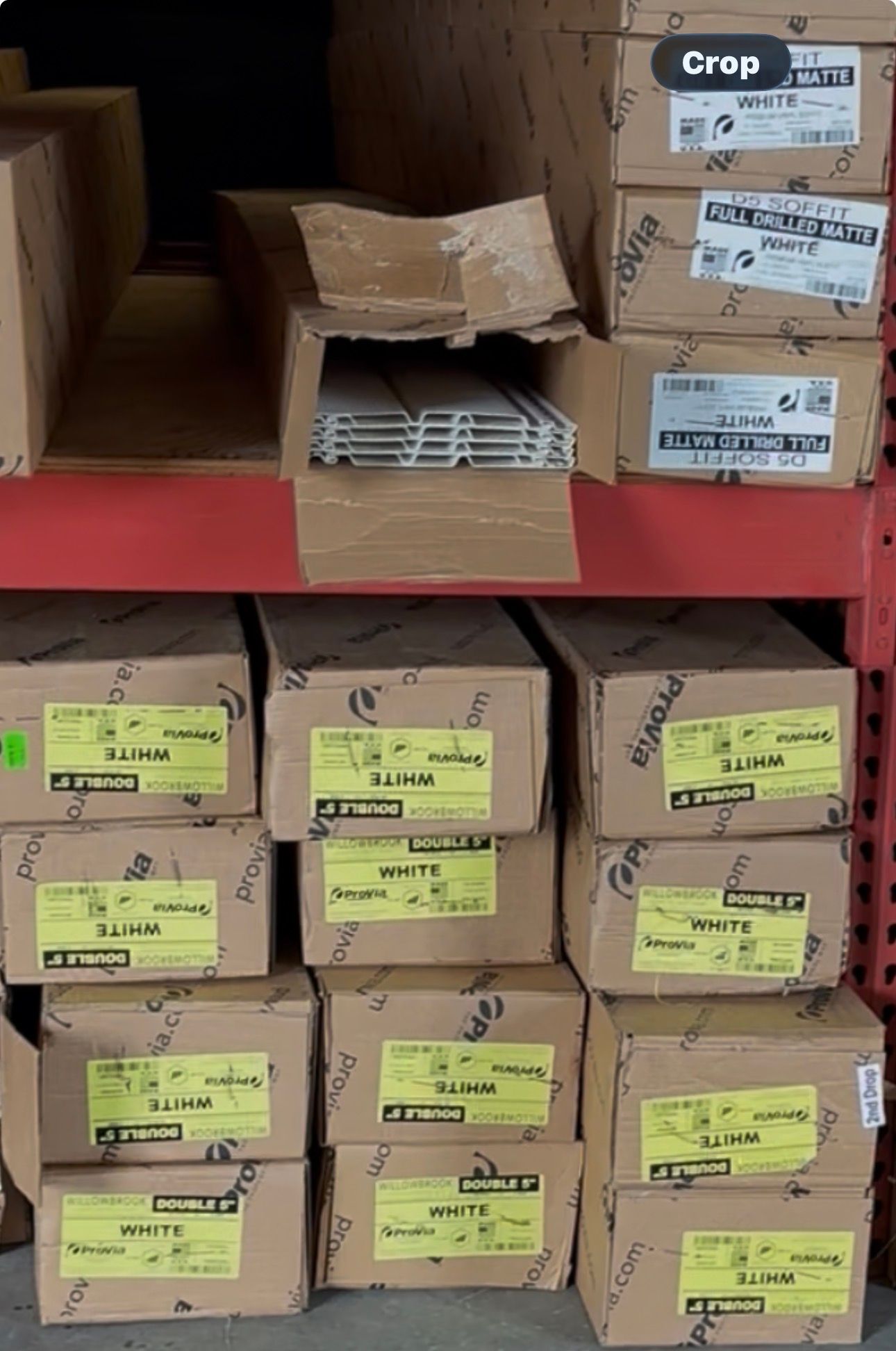 Cardboard boxes stacked on metal shelves in a storage area, with some yellow labels visible.
